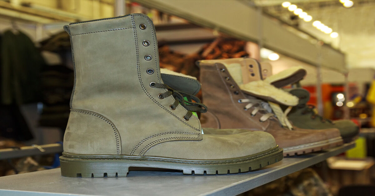 Three different army boots with fur lining, are displayed on a metal shelf. They are light green, brown, and dark green.